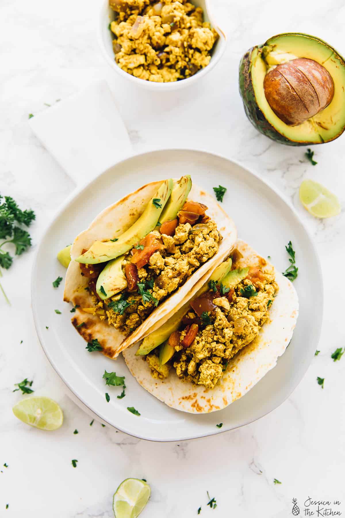 Top down view of tofu scramble in tortillas with lime wedges on the side. 