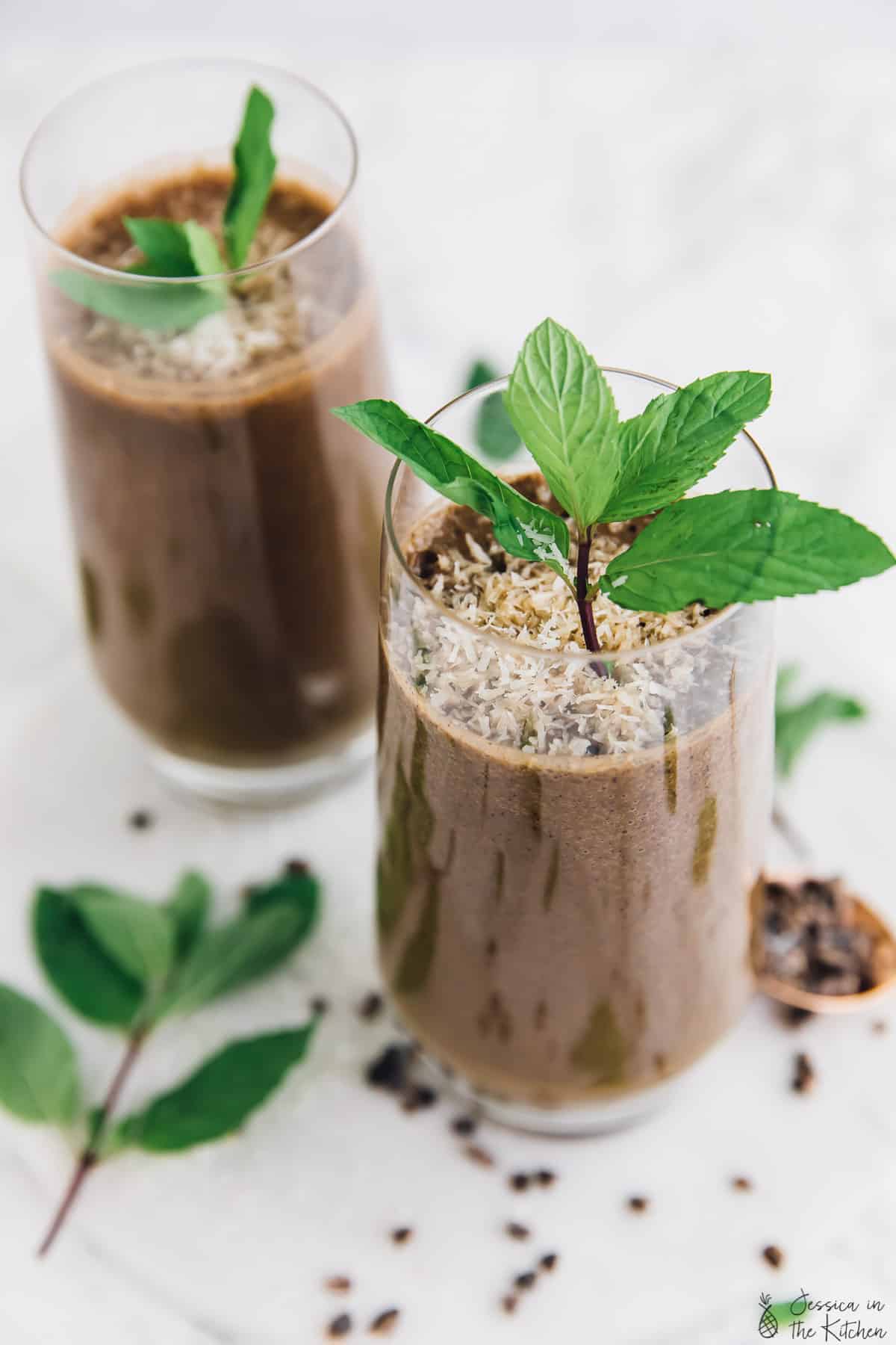 Two glasses of mint chocolate coffee shake, garnished with mint leaves. 