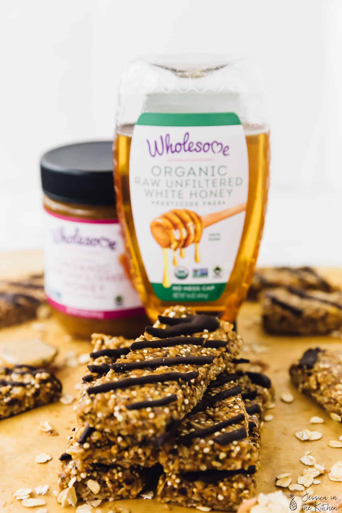 A stack of granola bars on a wooden board with a bottle of honey in the background. 