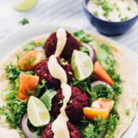 Beet falafels on pita with salad and dressing drizzled on top.