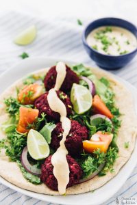 Beet falafels on pita with salad and dressing drizzled on top.