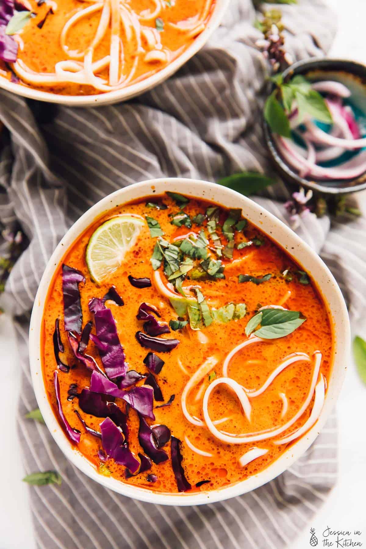 Overhead view of vegan coconut curry soup topped with red cabbage and a lime wedges. 