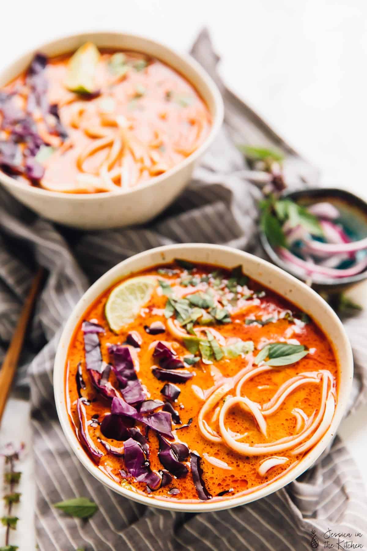 Two bowls of coconut curry soup on a grey cloth. 