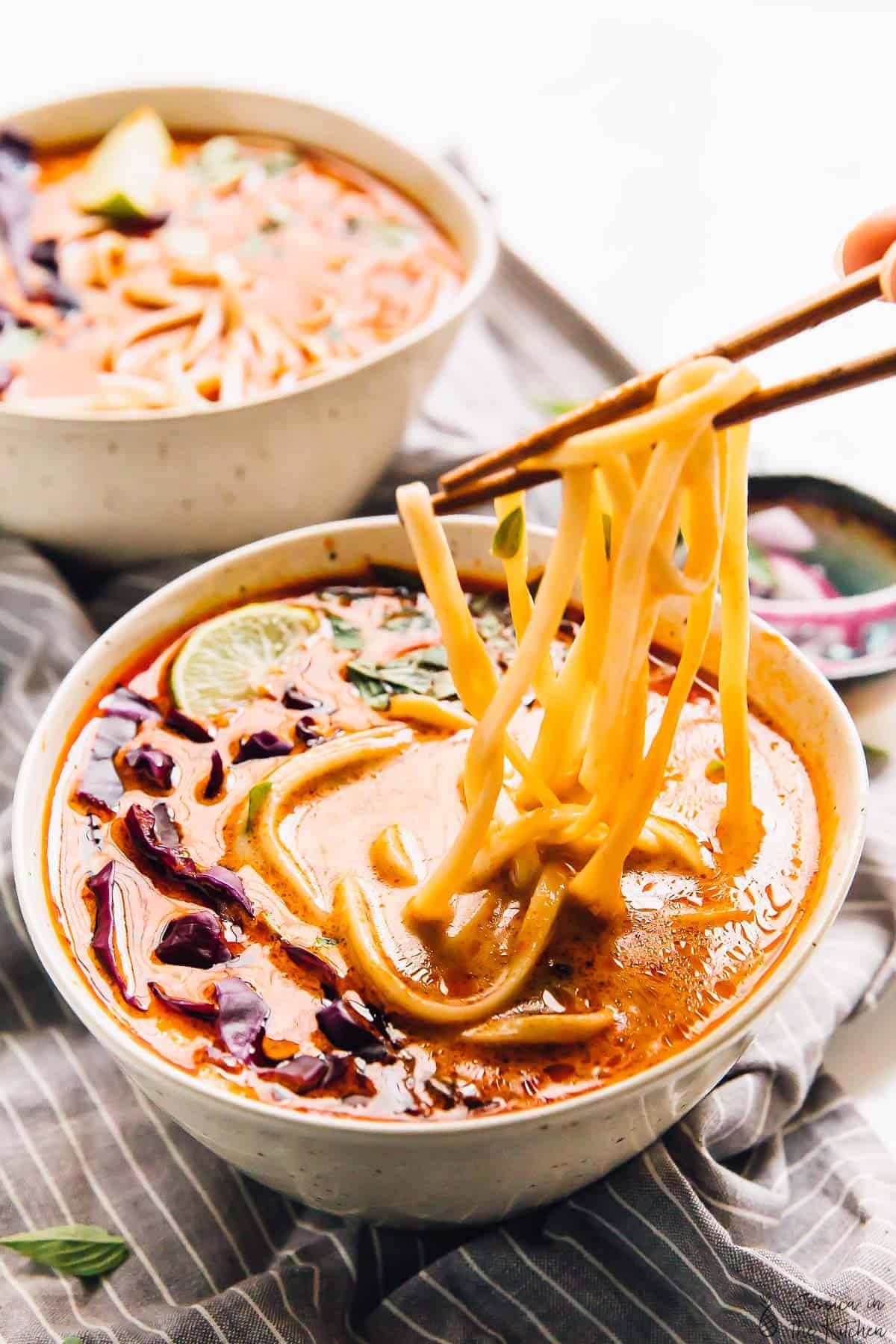 Chopsticks lifting noodles out of coconut curry soup.