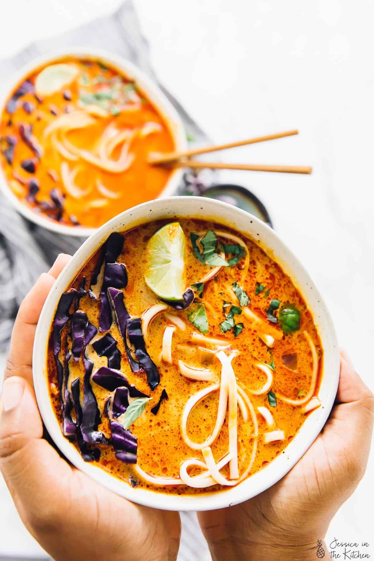 Hands holding a bowl of coconut curry soup.