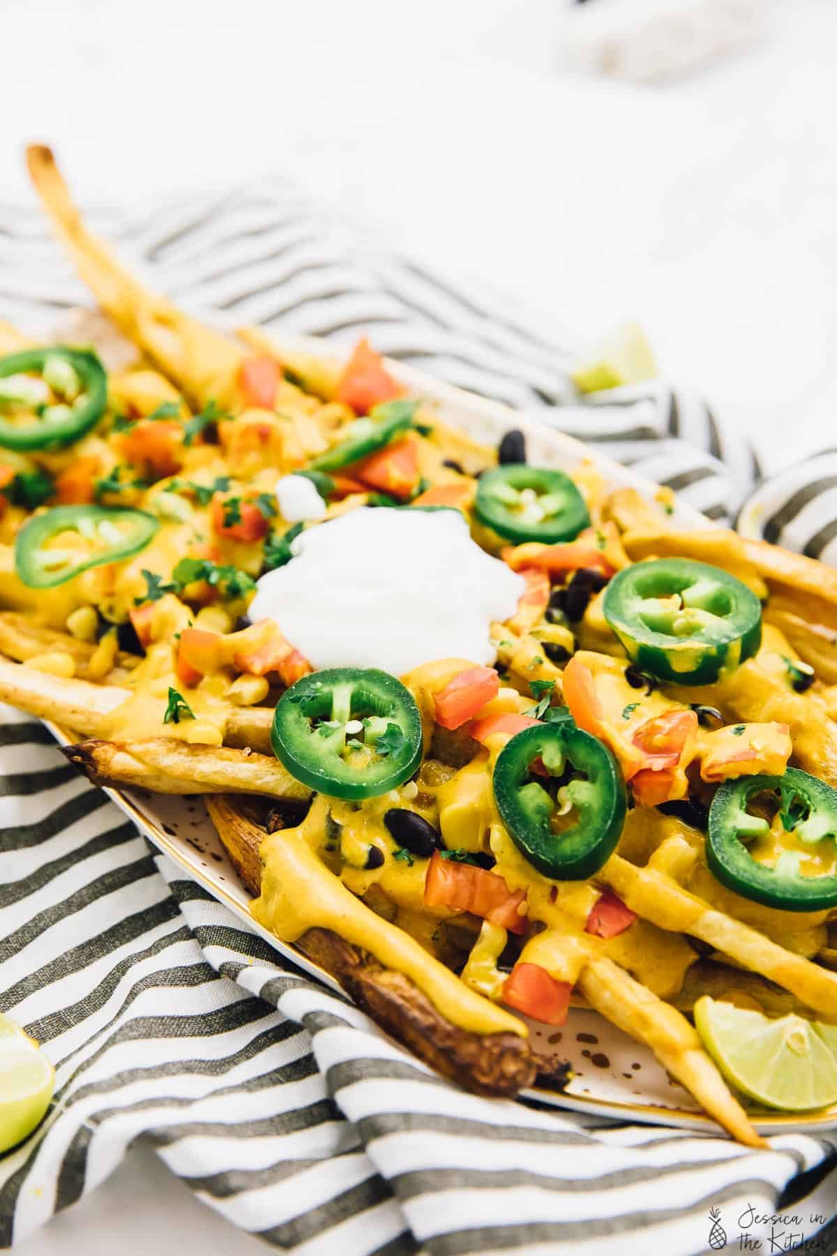 Vegan loaded nacho cheese fries topped with sliced jalapeno, on a long plate. 