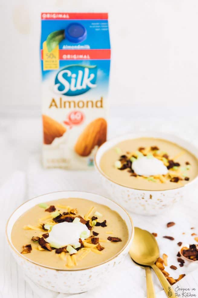 Two bowls of loaded potato soup with a carton of nut milk in the background.