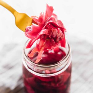 Purple quick pickled cabbage held up by a fork over a jar of more quick pickled cabbage in a glass jar.