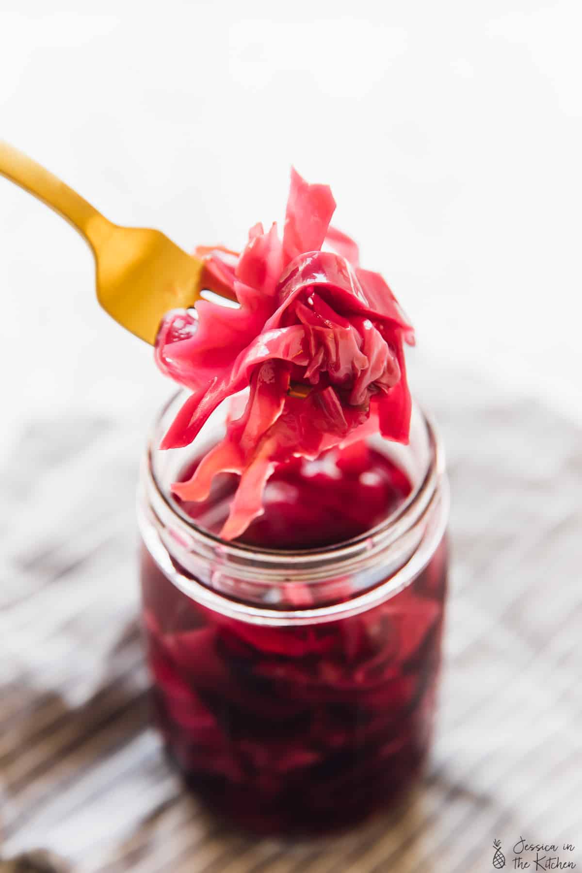 Purple quick pickled cabbage held up by a fork over a jar of more quick pickled cabbage. 