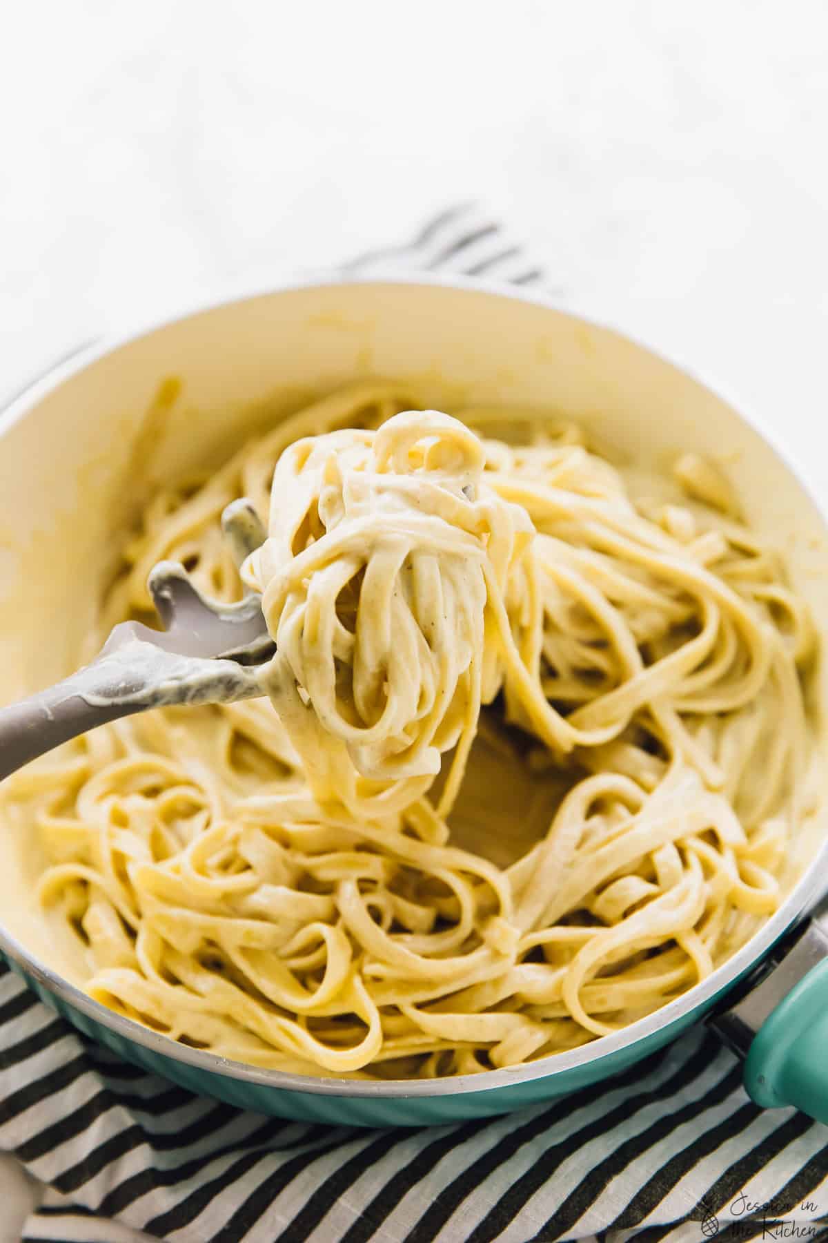 Pasta spoon scooping vegan garlic Alfredo pasta out of a pot.