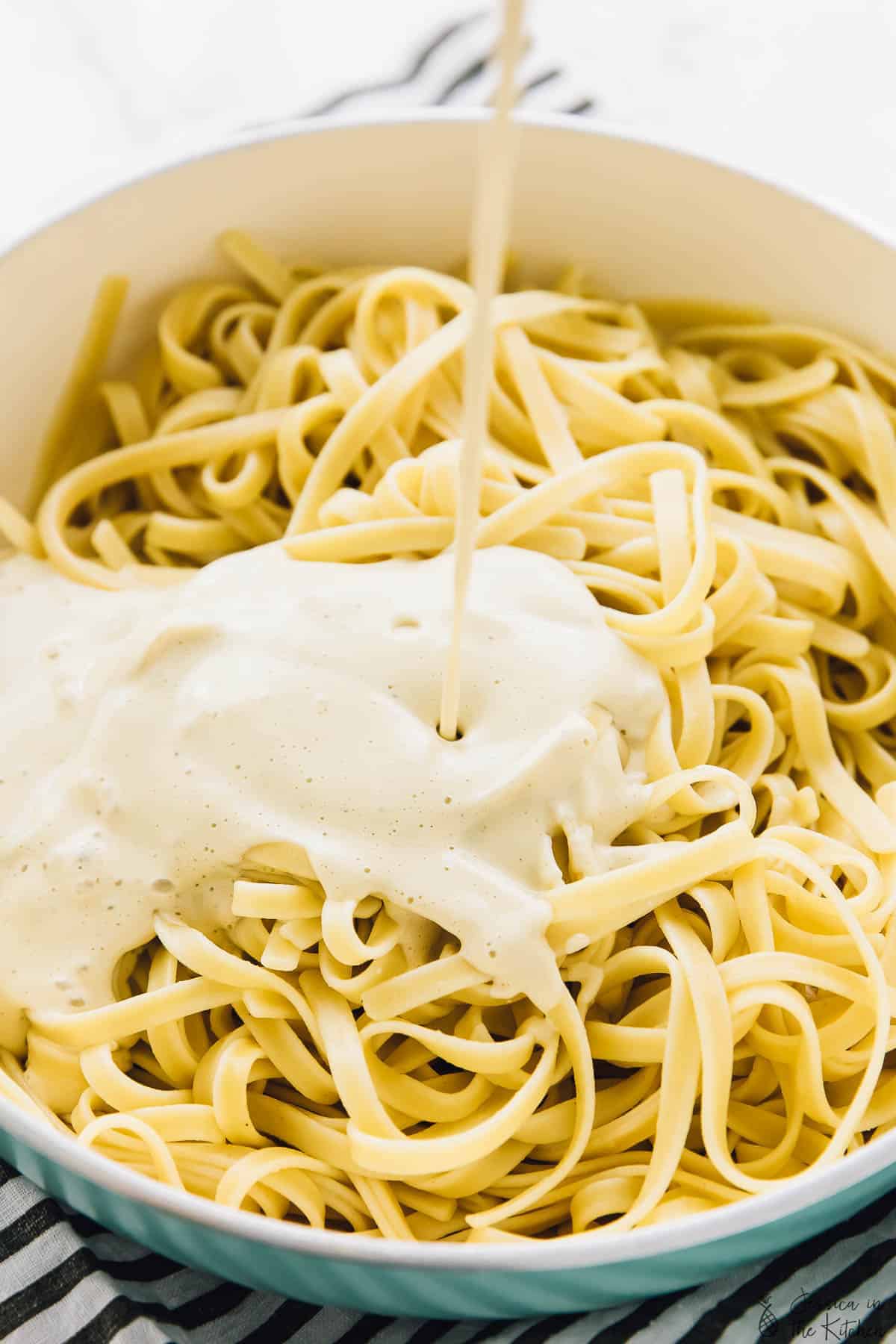 Alfredo sauce being poured on to a pot of pasta to make vegan garlic Alfredo pasta. 