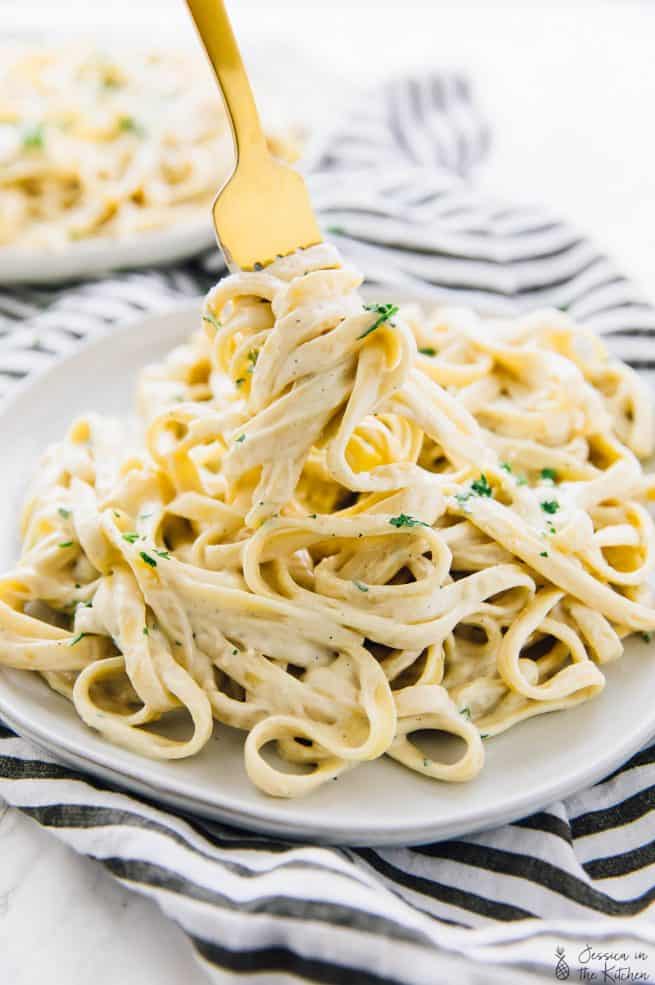 Vegan garlic Alfredo pasta on plate being twirled by a gold fork.