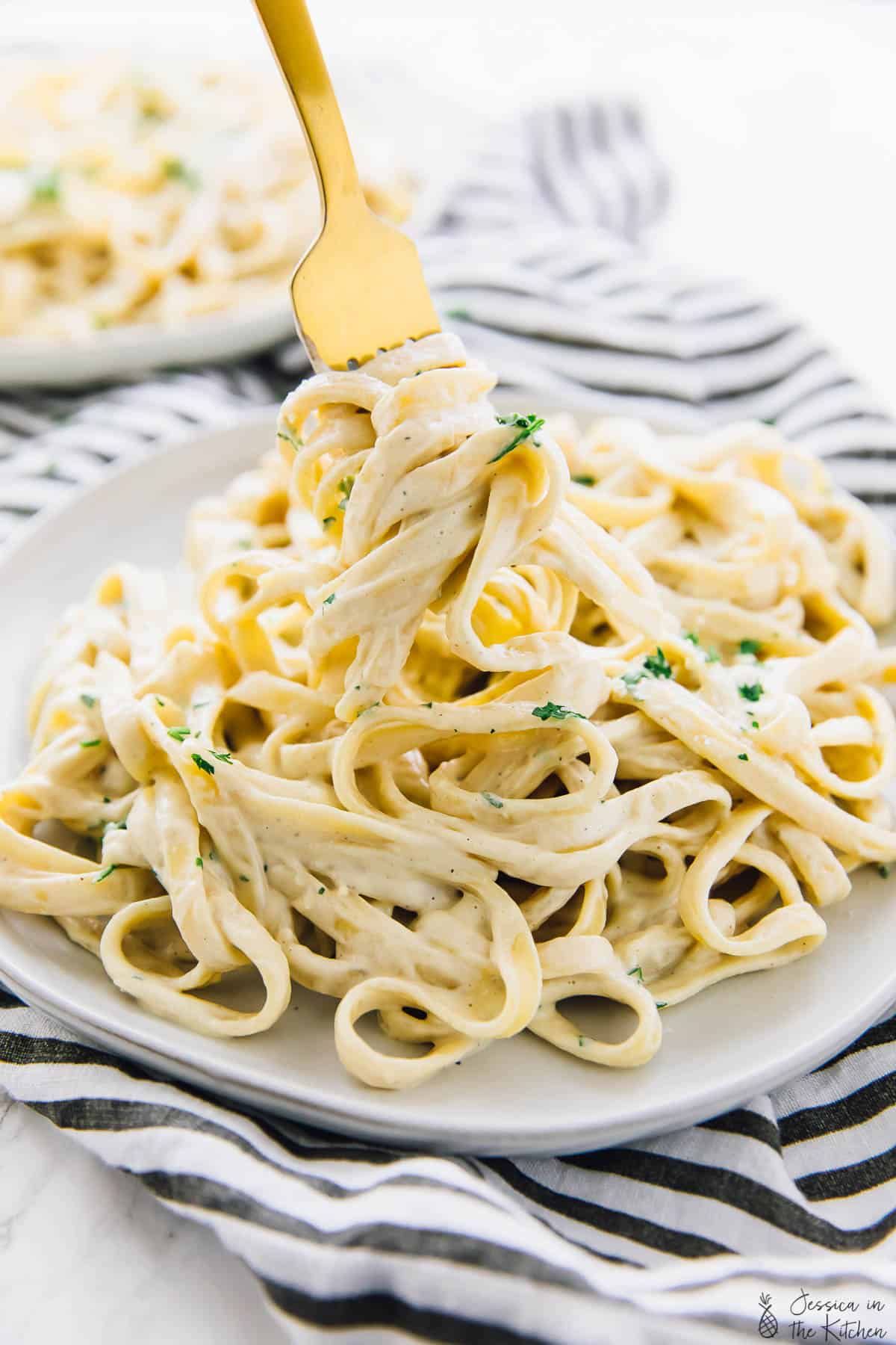 A fork digging into a plate of pasta covered in vegan garlic alfredo sauce.