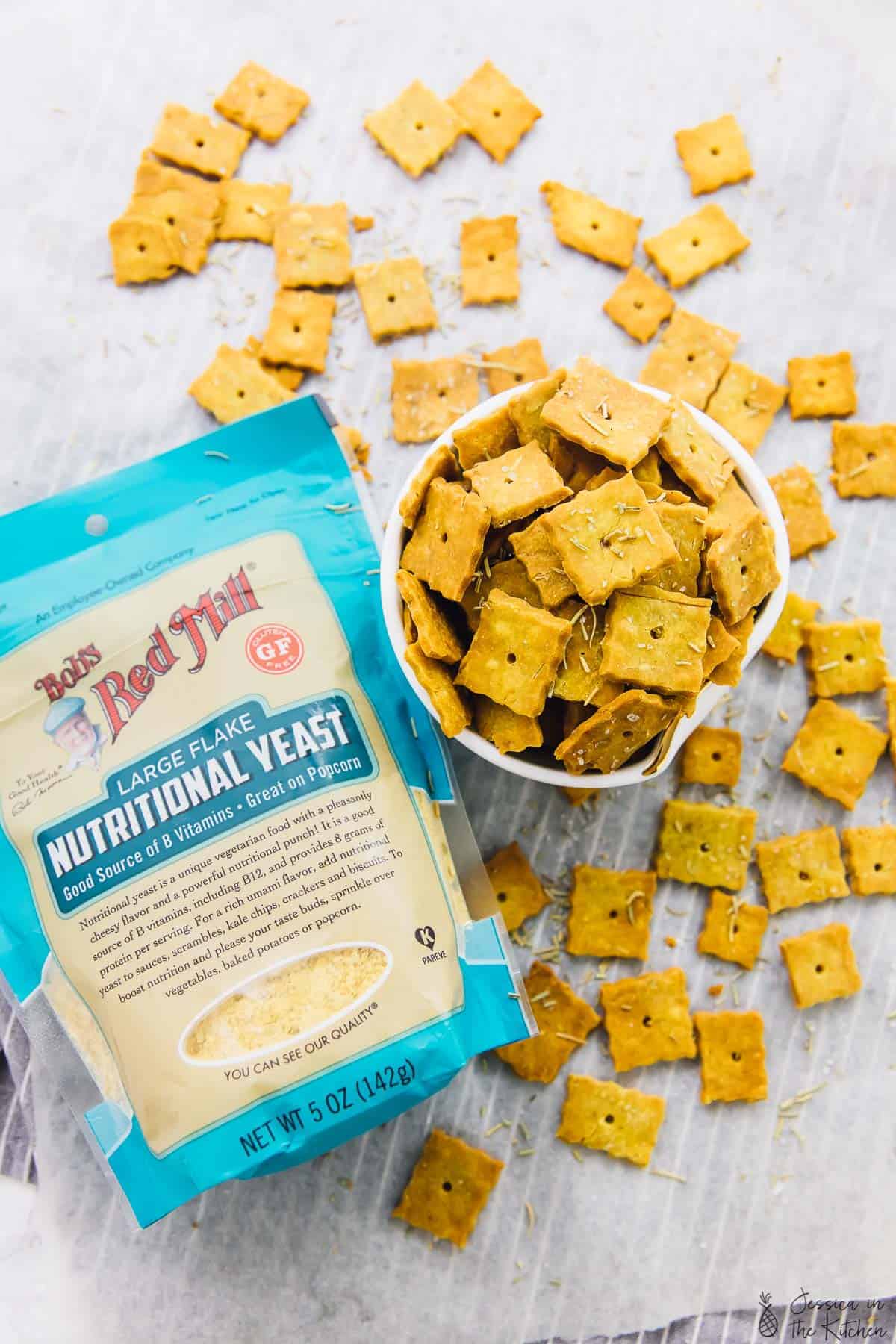 Overhead view of vegan herbed parmesan crackers in a bowl with a pack of nutritional yeast next to it. 