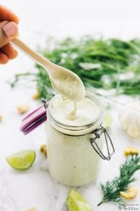 A spoon dipping into ranch dressing in a jar.
