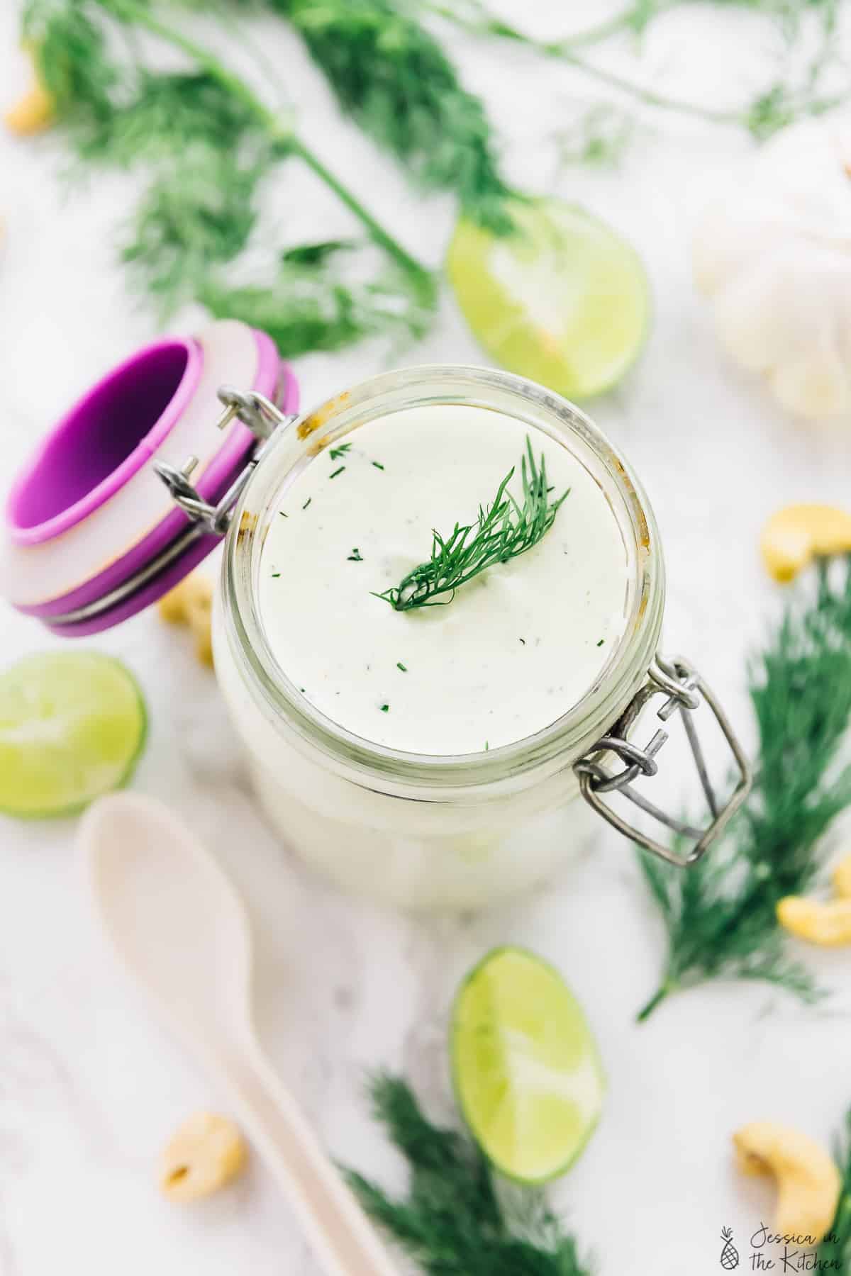 Overhead view of vegan ranch dressing in a glass jar, surrounded by herbs.