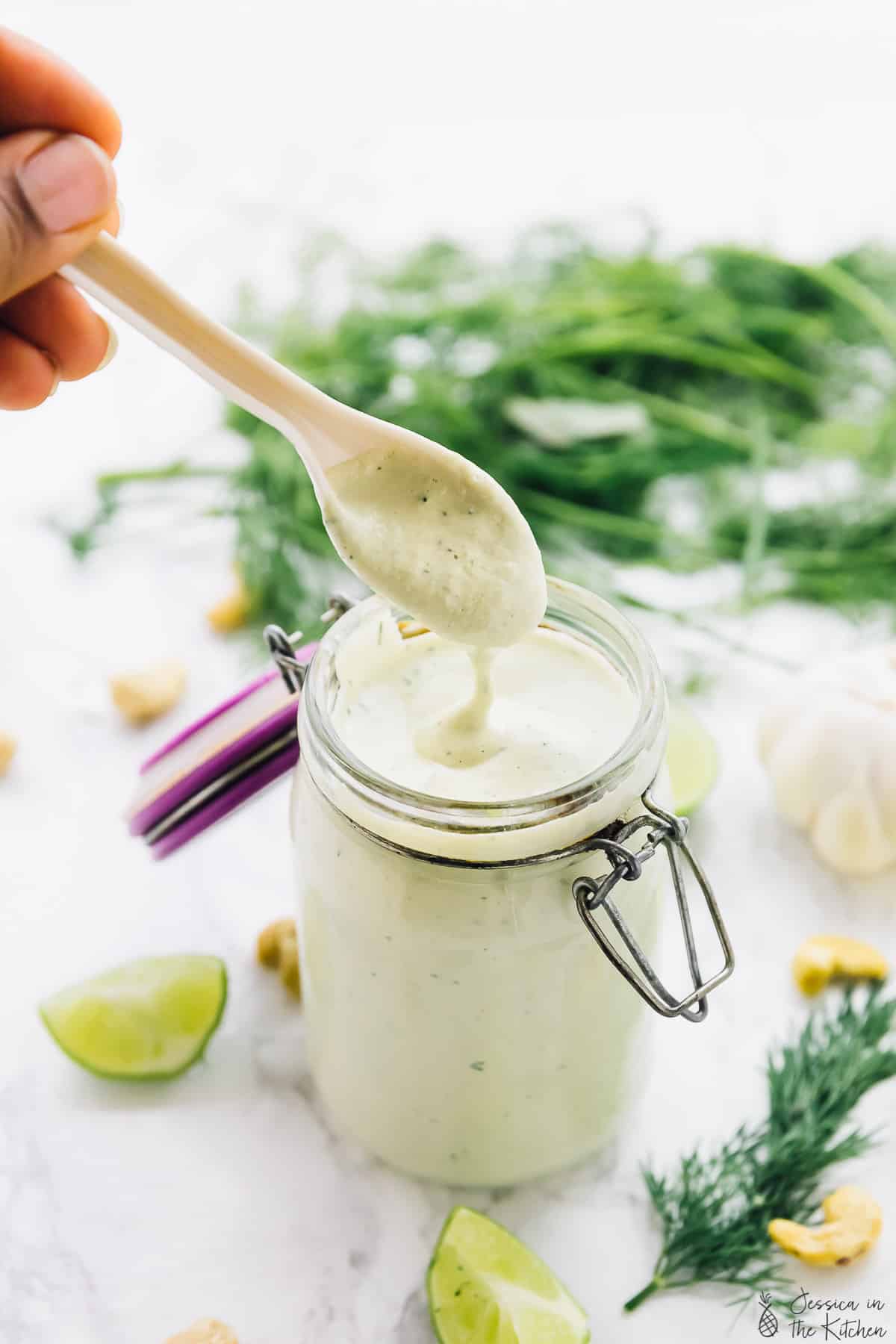A hand dipping a spoon into vegan ranch dressing.