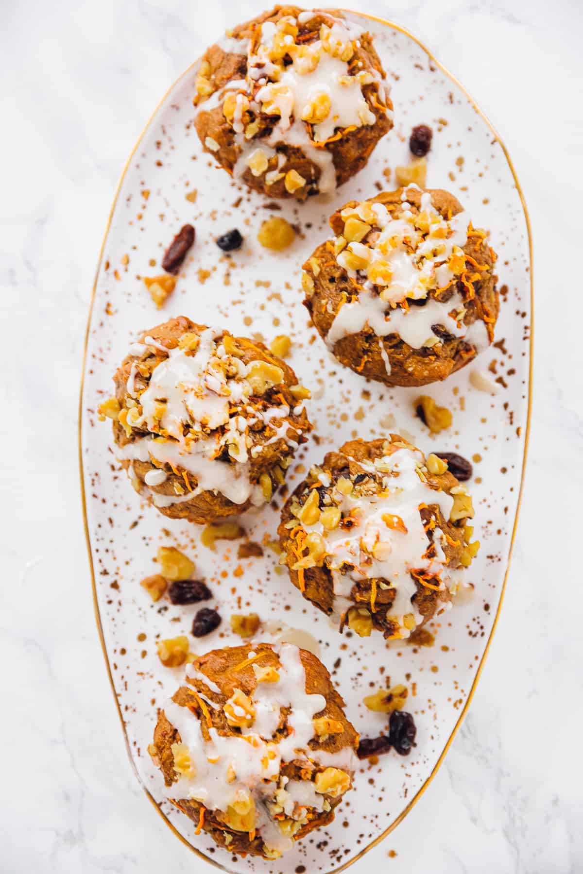 overhead shot of carrot cake muffins with icing lined up on a white and gold plate