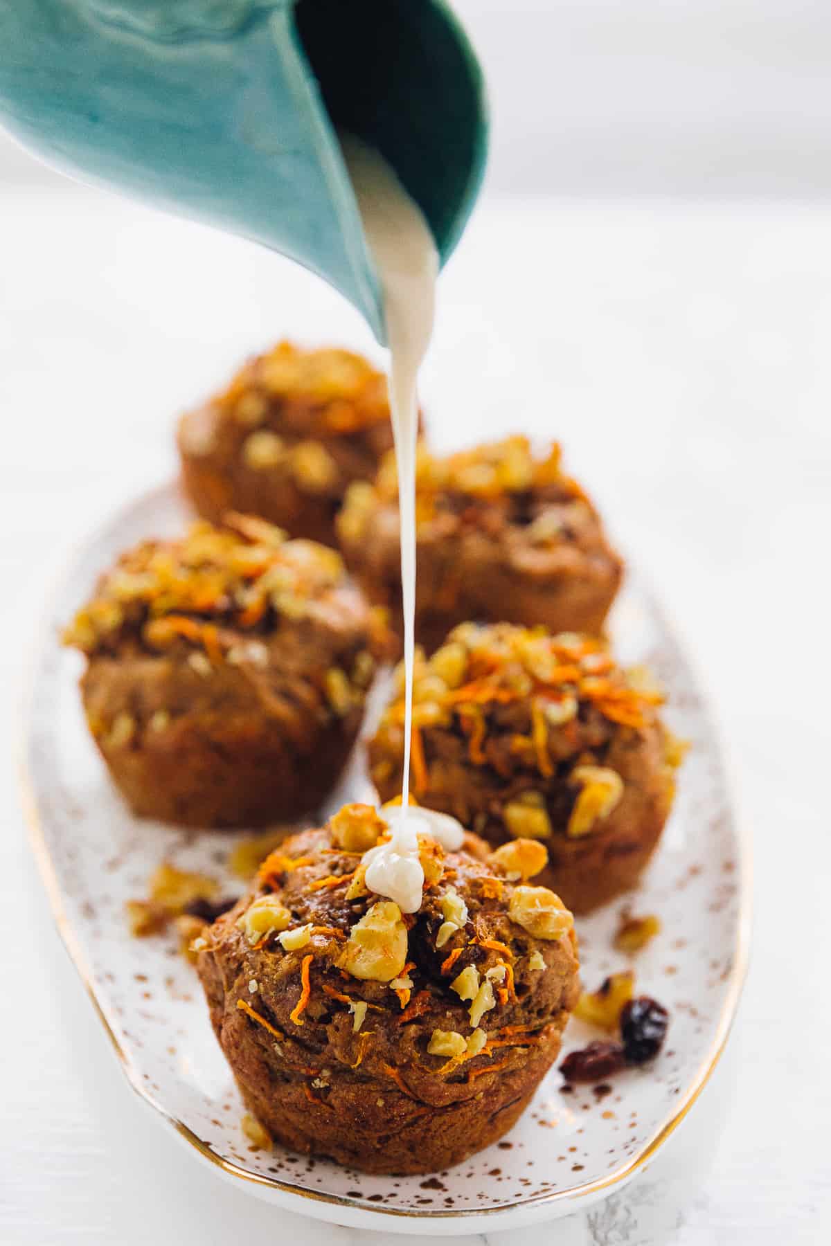 Icing being poured on a carrot cake muffin. 