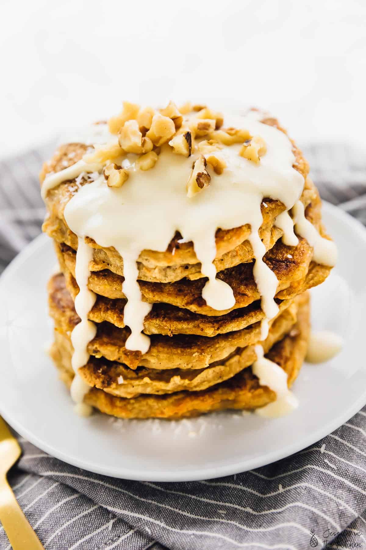 A stack of vegan carrot cake pancakes, covered in sauce. 