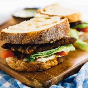 A vegan blt, cut in half, on a wood board.