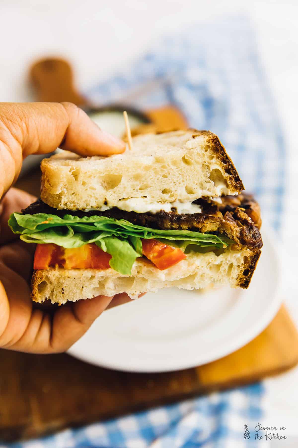 Person holding half of a vegan BLT sandwich.