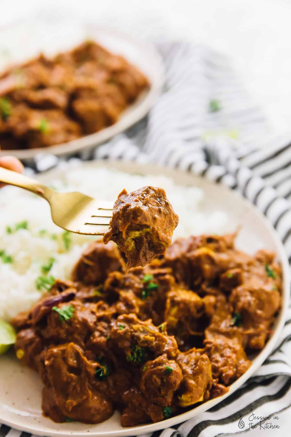 A fork holding up a piece of butter chicken.