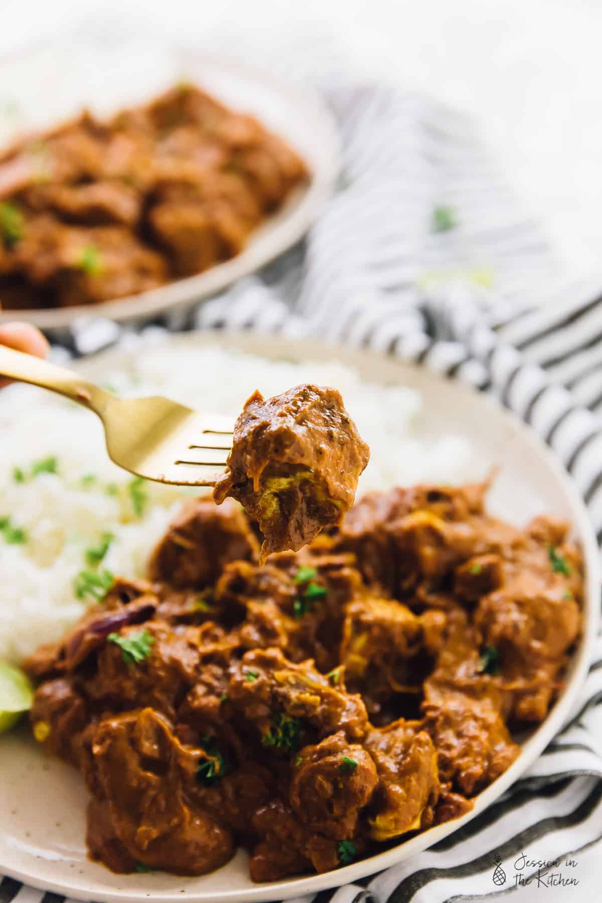 A fork with some vegan butter chicken, in front of a plate of vegan butter chicken.