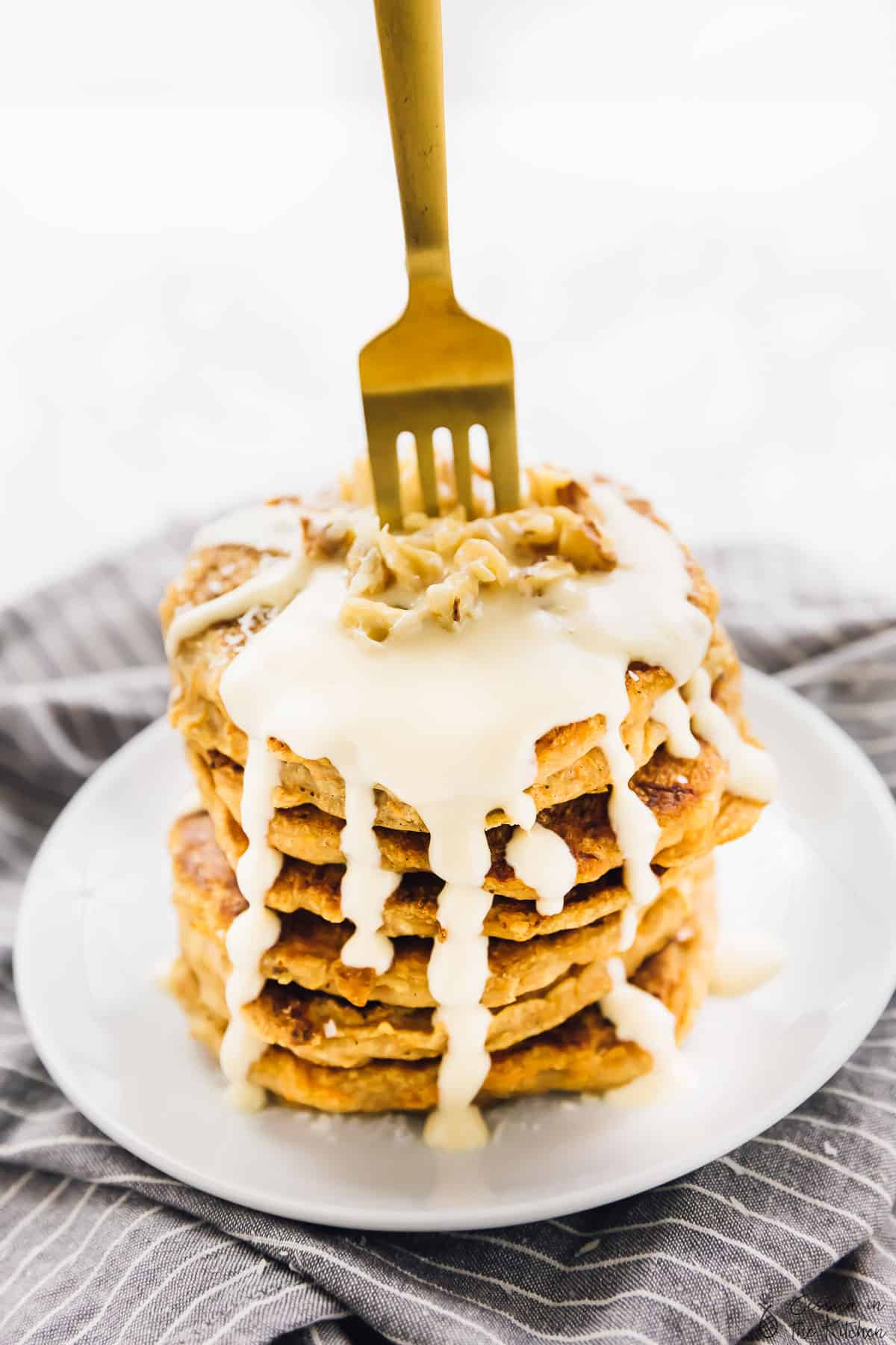 A gold fork in a stack of pancakes.