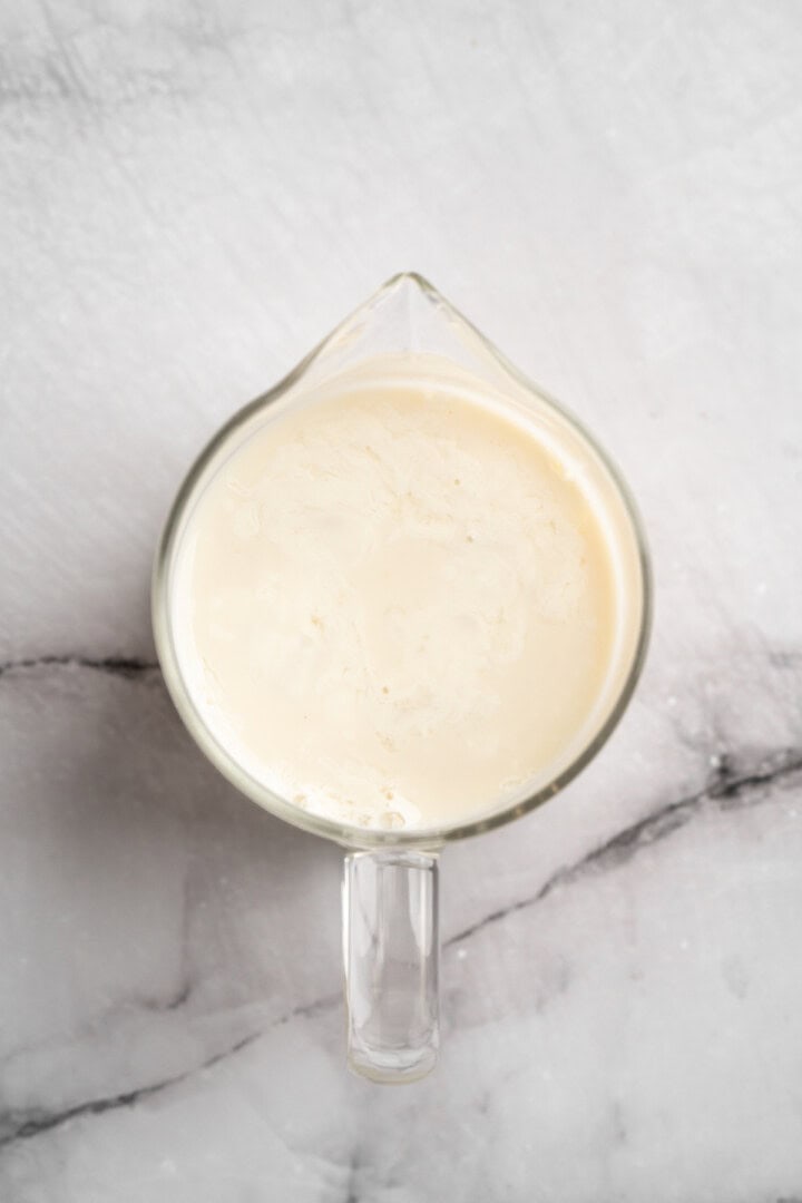 These carrot cake pancakes are fluffy, warmly spiced, and topped with an irresistible maple cream cheese drizzle. A cozy vegan breakfast! Vegan buttermilk in liquid measuring cup.