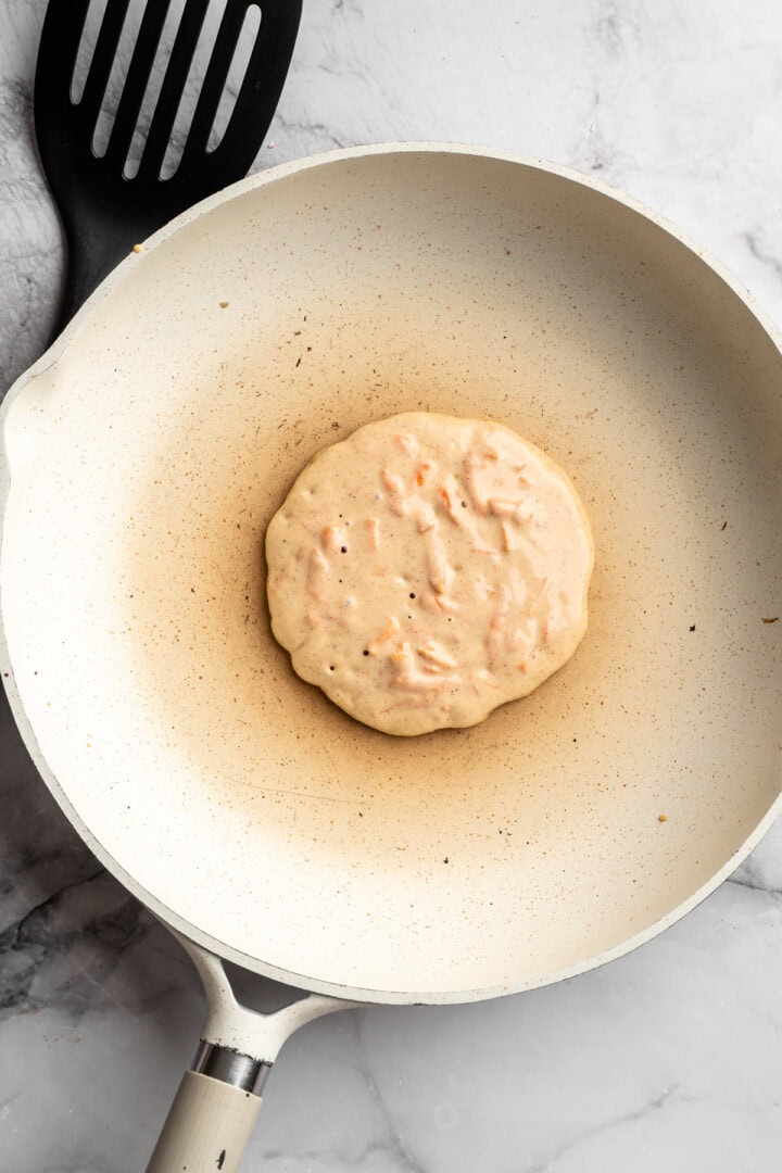These carrot cake pancakes are fluffy, warmly spiced, and topped with an irresistible maple cream cheese drizzle. A cozy vegan breakfast! Carrot cake pancake in skillet before flipping.