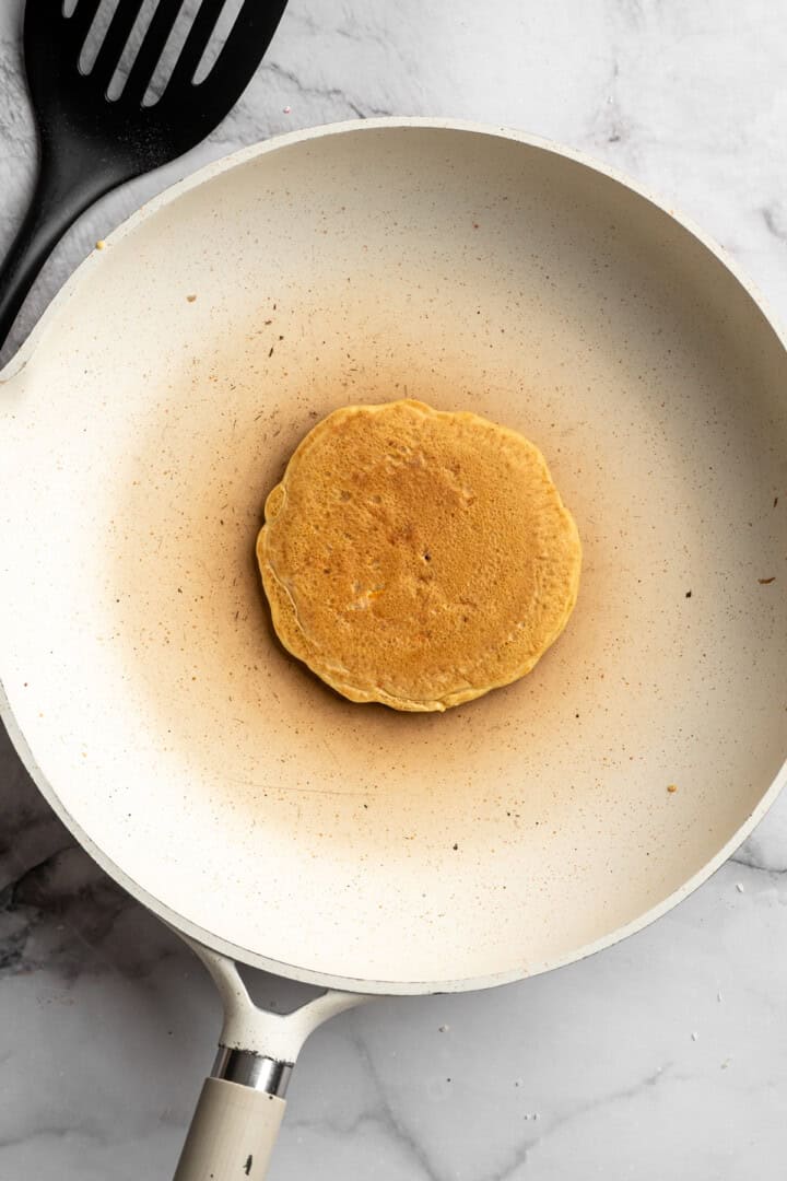 These carrot cake pancakes are fluffy, warmly spiced, and topped with an irresistible maple cream cheese drizzle. A cozy vegan breakfast! Carrot cake pancake in skillet.