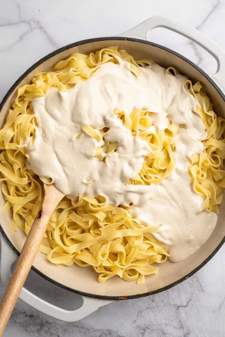 Overhead view of vegan Alfredo sauce added over skillet of fettuccine