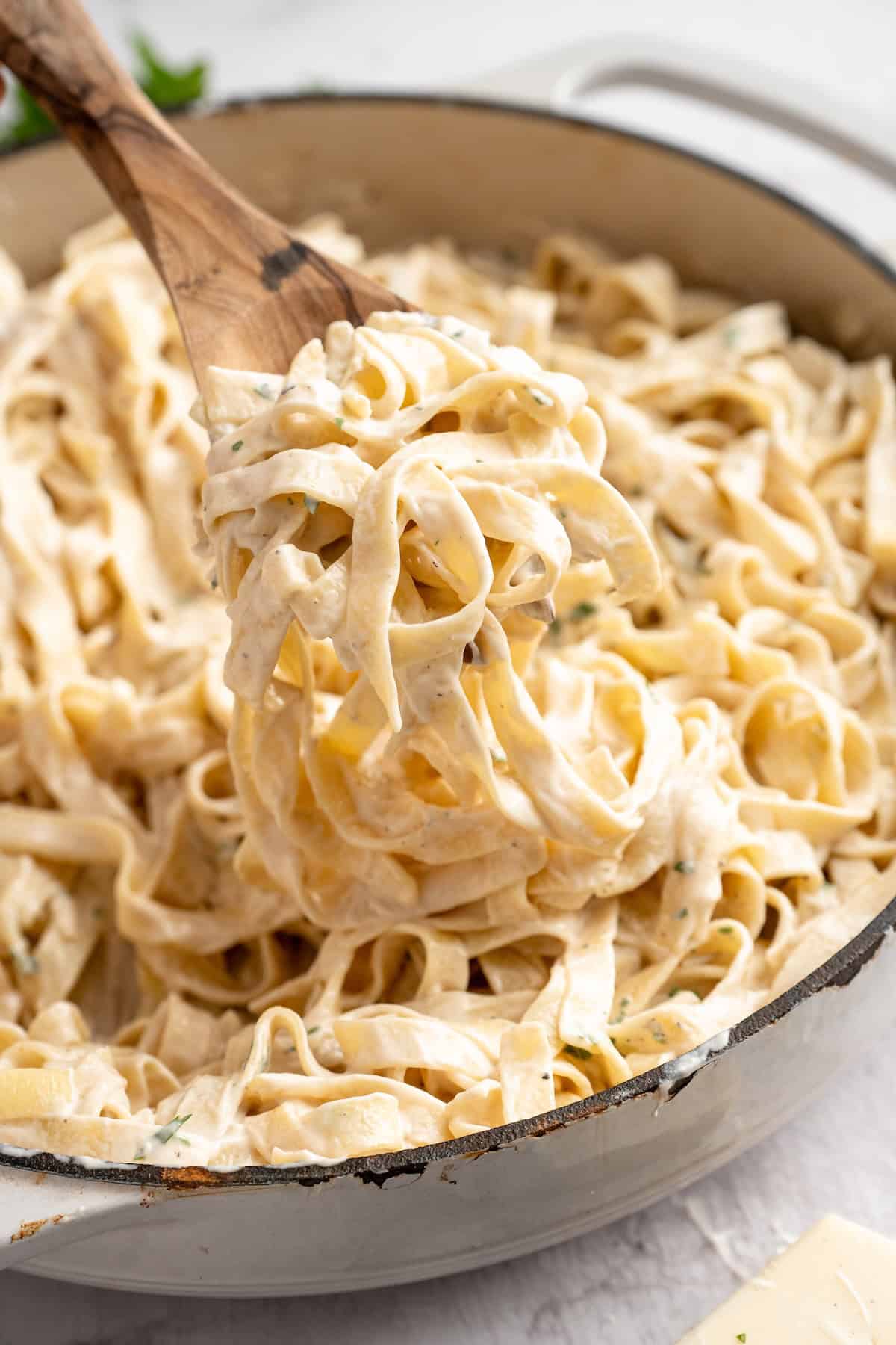 Lifting vegan garlic Alfredo pasta from skillet with wooden spoon