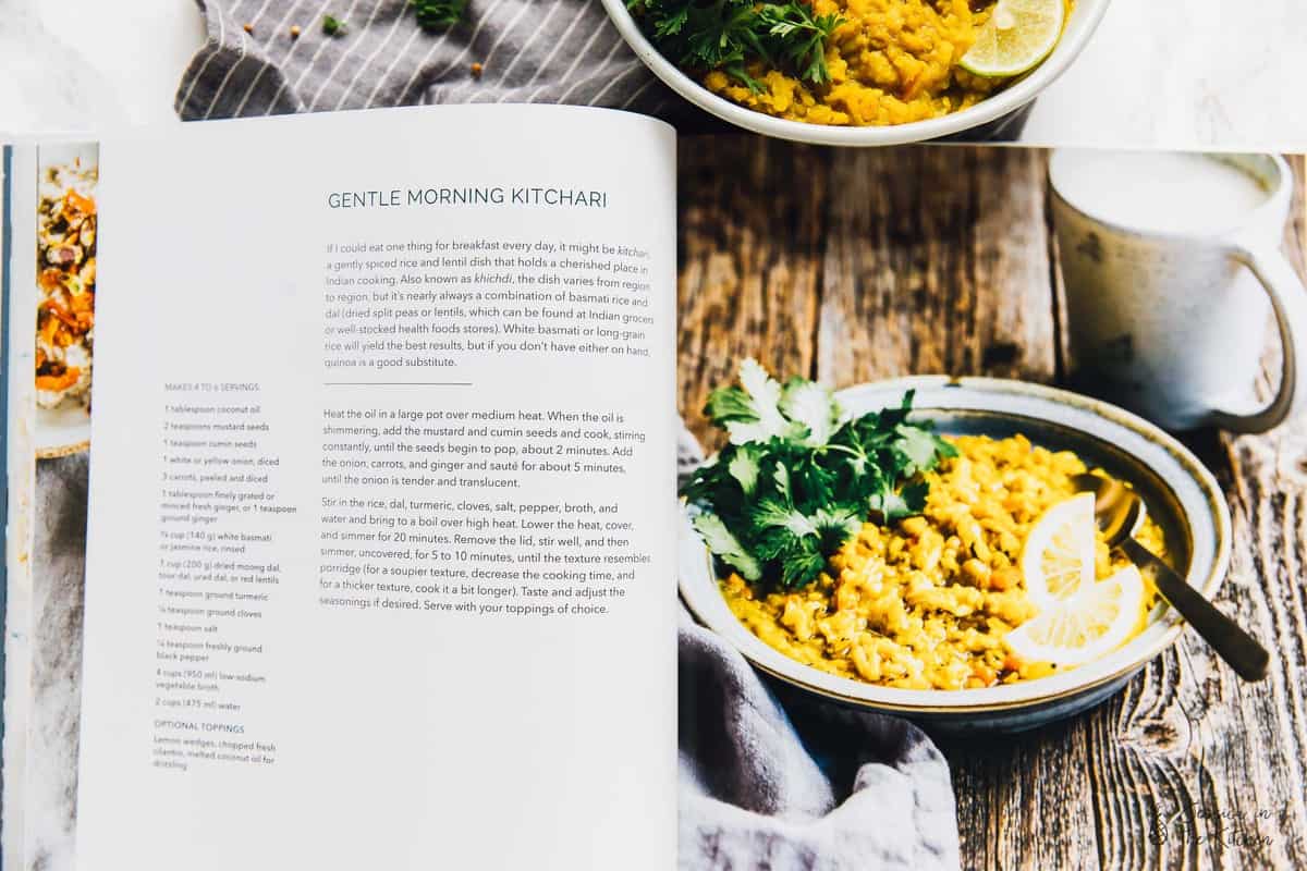 A cookbook opened to a picture and recipe called "gentle morning kitchar," with a bowl of kitchari behind it