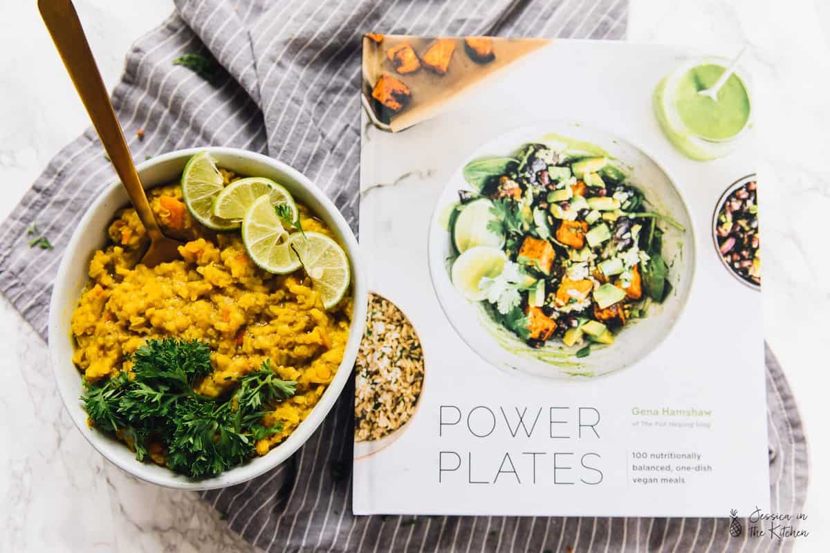 A bowl of kitchari topped with lime and parsley, with a spoon in it, next to a cookbook called "Power Plates"