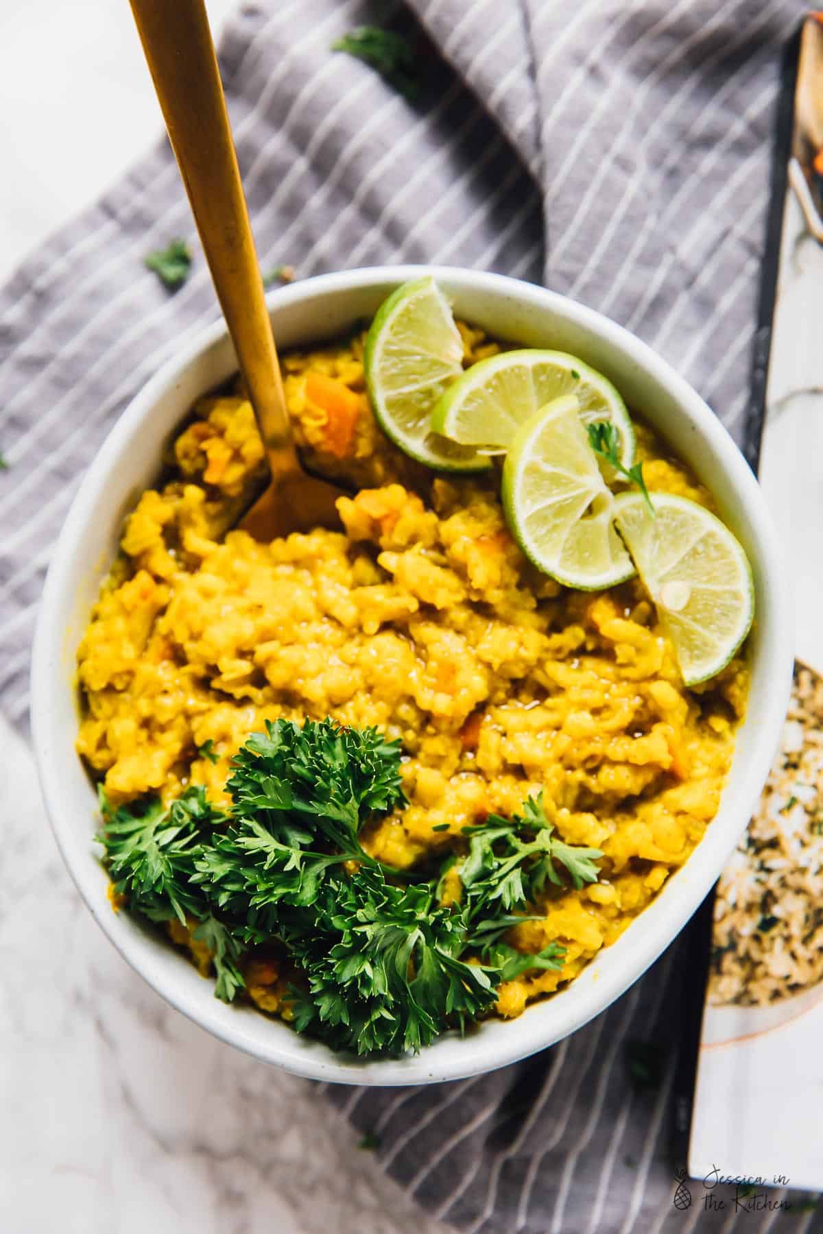 Overhead view of a bowl of kitchari topped with parsley and lime slices, with a spoon sticking out of it