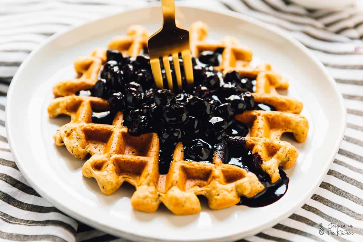 A gold fork sticking into a lemon poppyseed waffle.