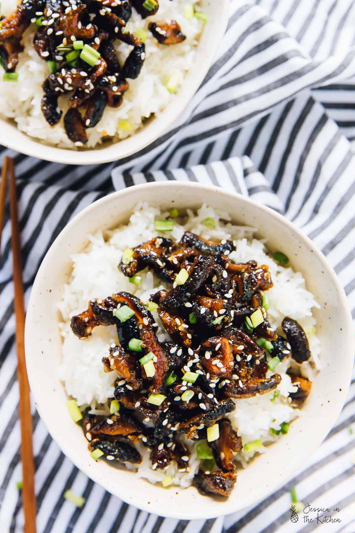 Overhead view sticky sesame shiitake mushrooms on a bed of rice with chopsticks on the side. 
