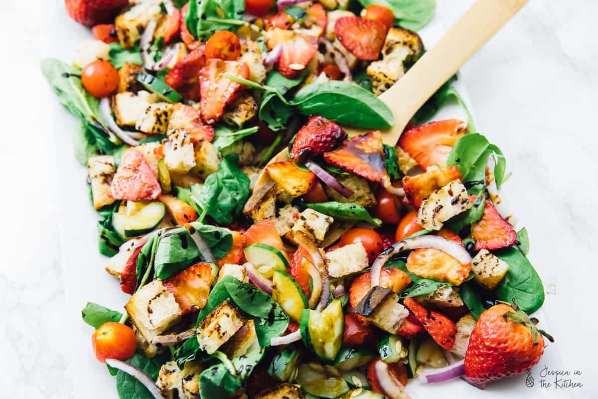 A wooden spoon in strawberry panzanella salad.