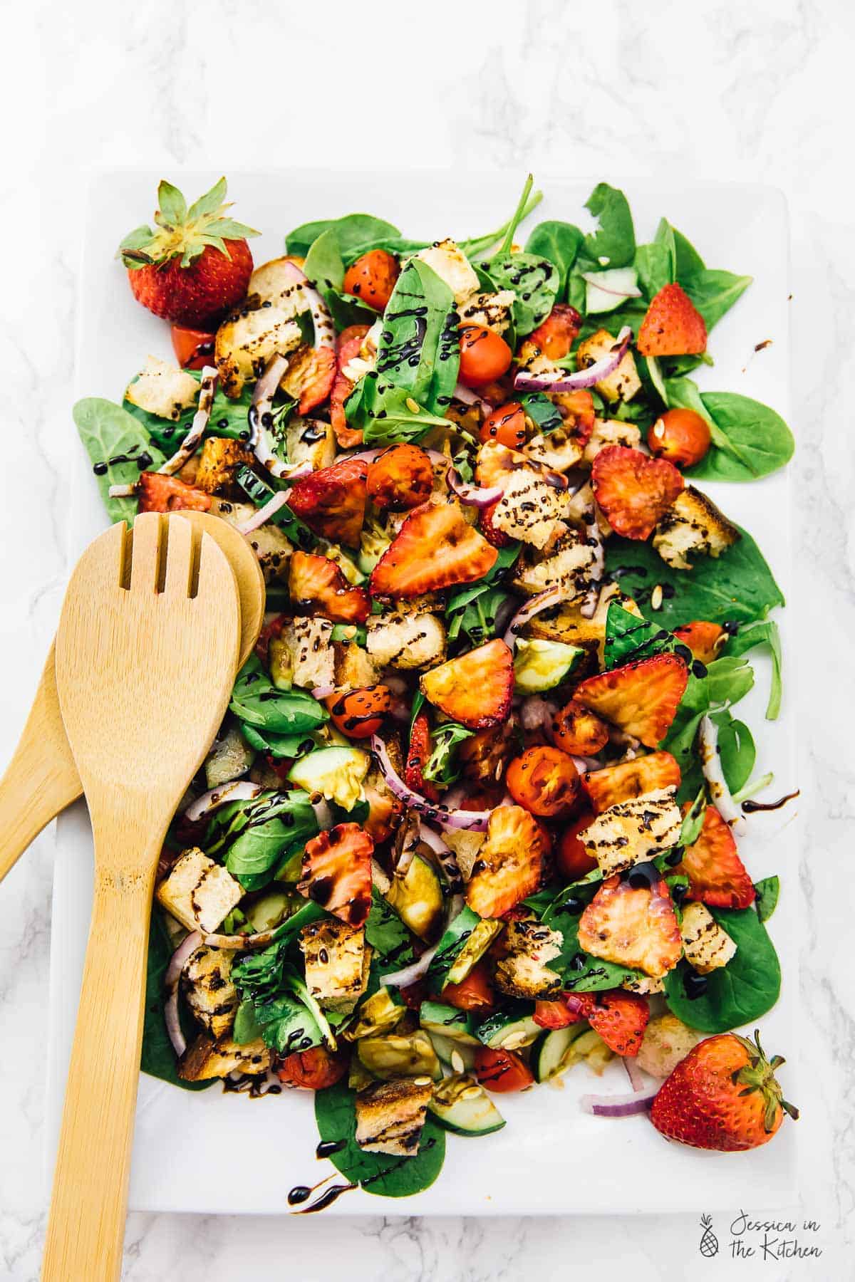 Overhead view of strawberry panzanella salad on square white plate.