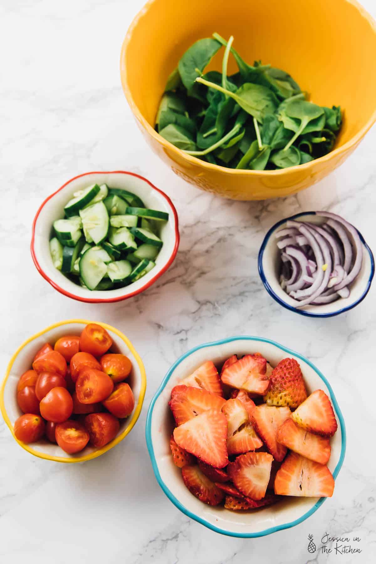 Top down view of chopped strawberries, cherry tomatoes, cucumbers, onions and spinach. 