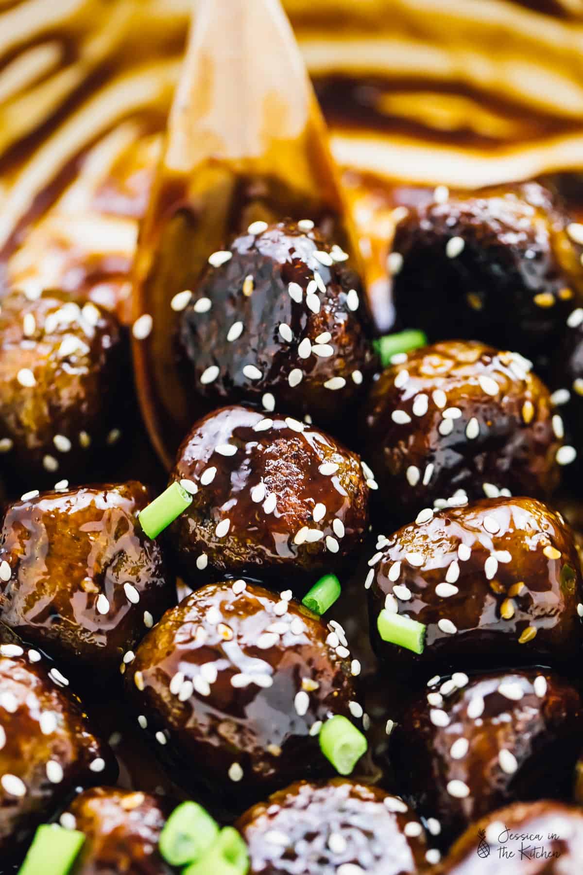 Vegan teriyaki meatballs being stirred by a wood spoon. 