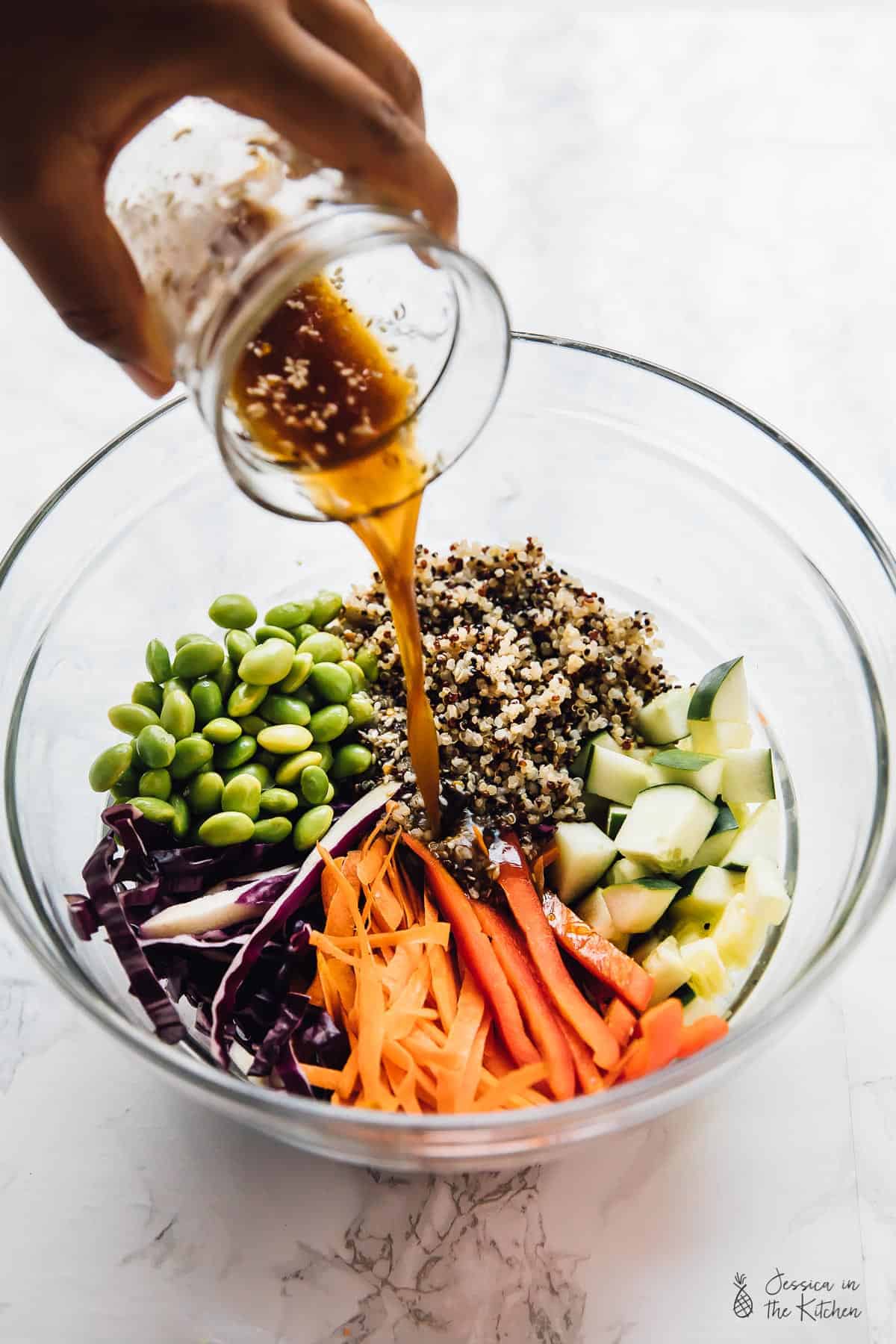 Pouring dressing into bowl of quinoa salad ingredients