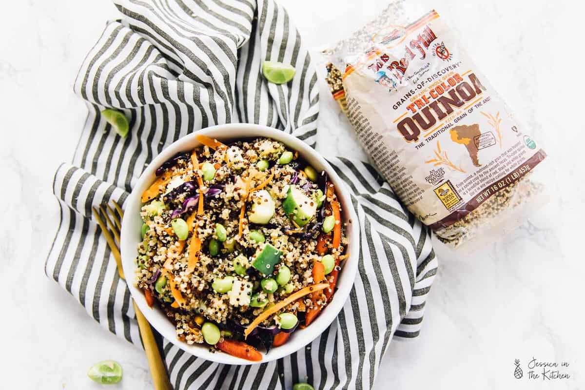 Bowl of Asian quinoa salad set next to bag of tri-color quinoa