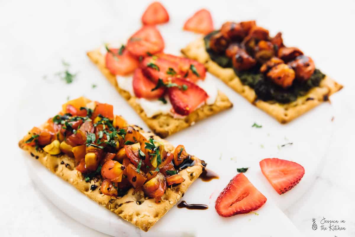Three crisp breads with toppings on a plate. 