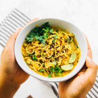 Hands holding a curried satay veggie bowl.