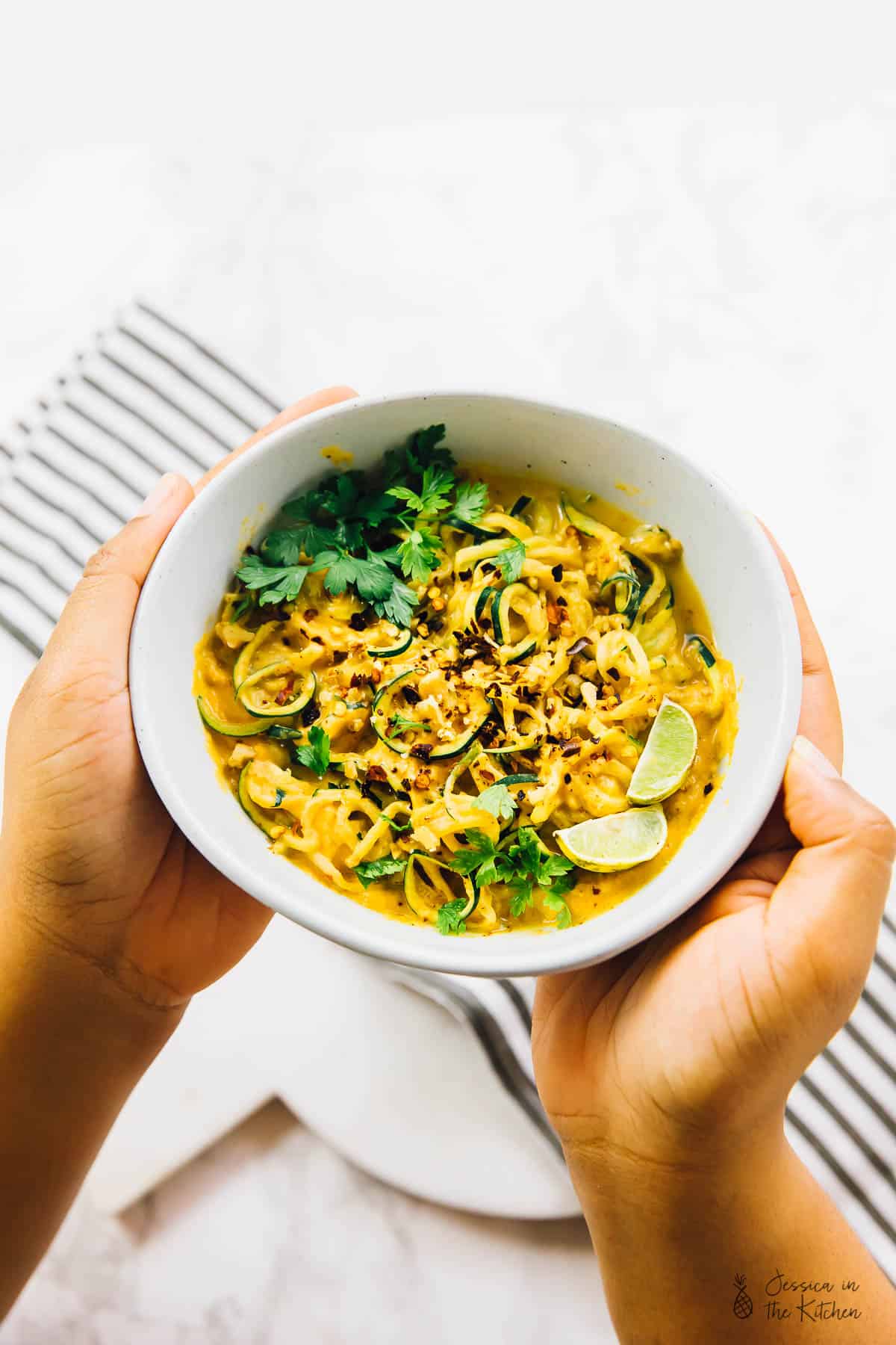 Hands holding a bowl of curried satay veggies.