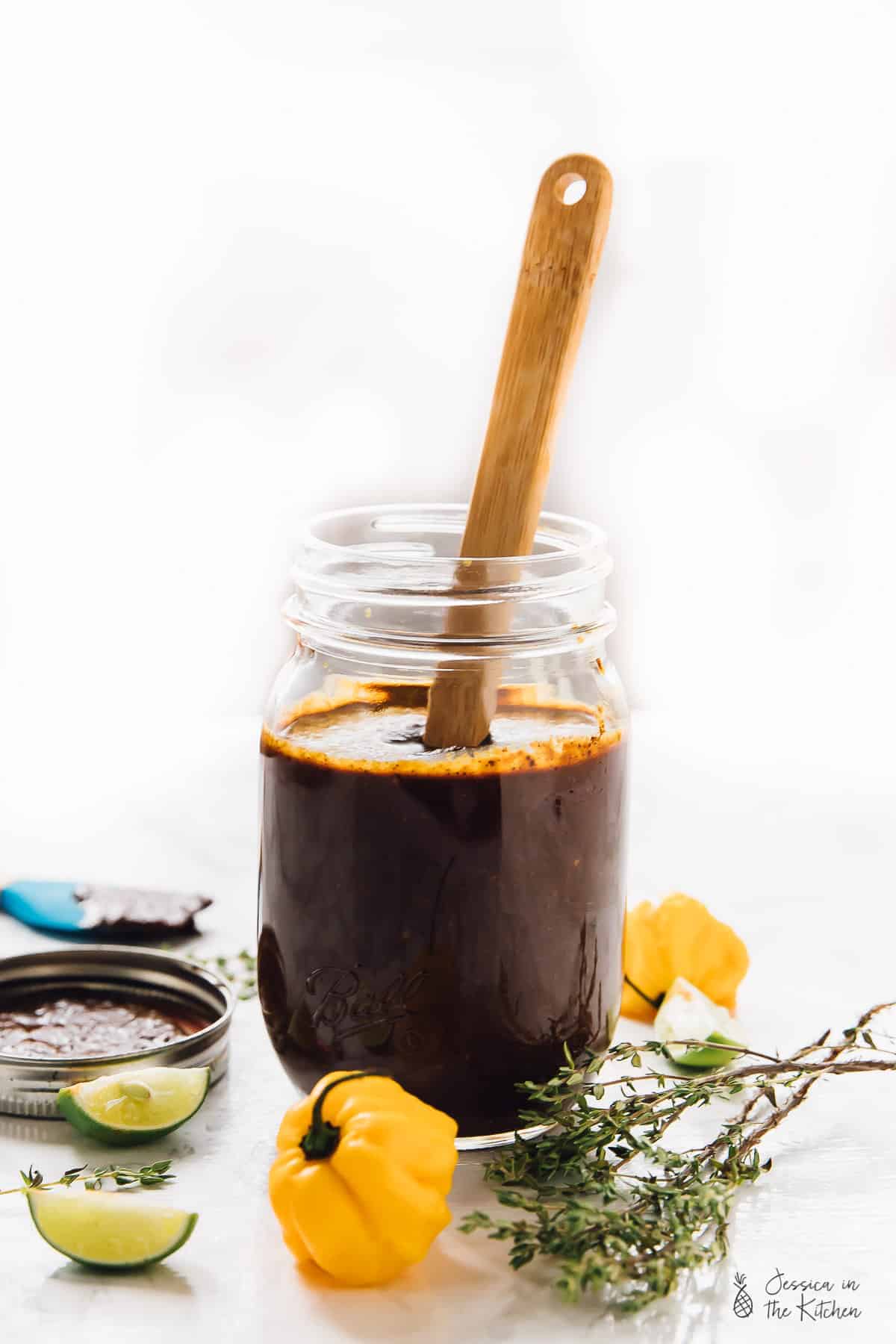 Jamaica Jerk Sauce in a jar in-front of scotch bonnet peppers and thyme.