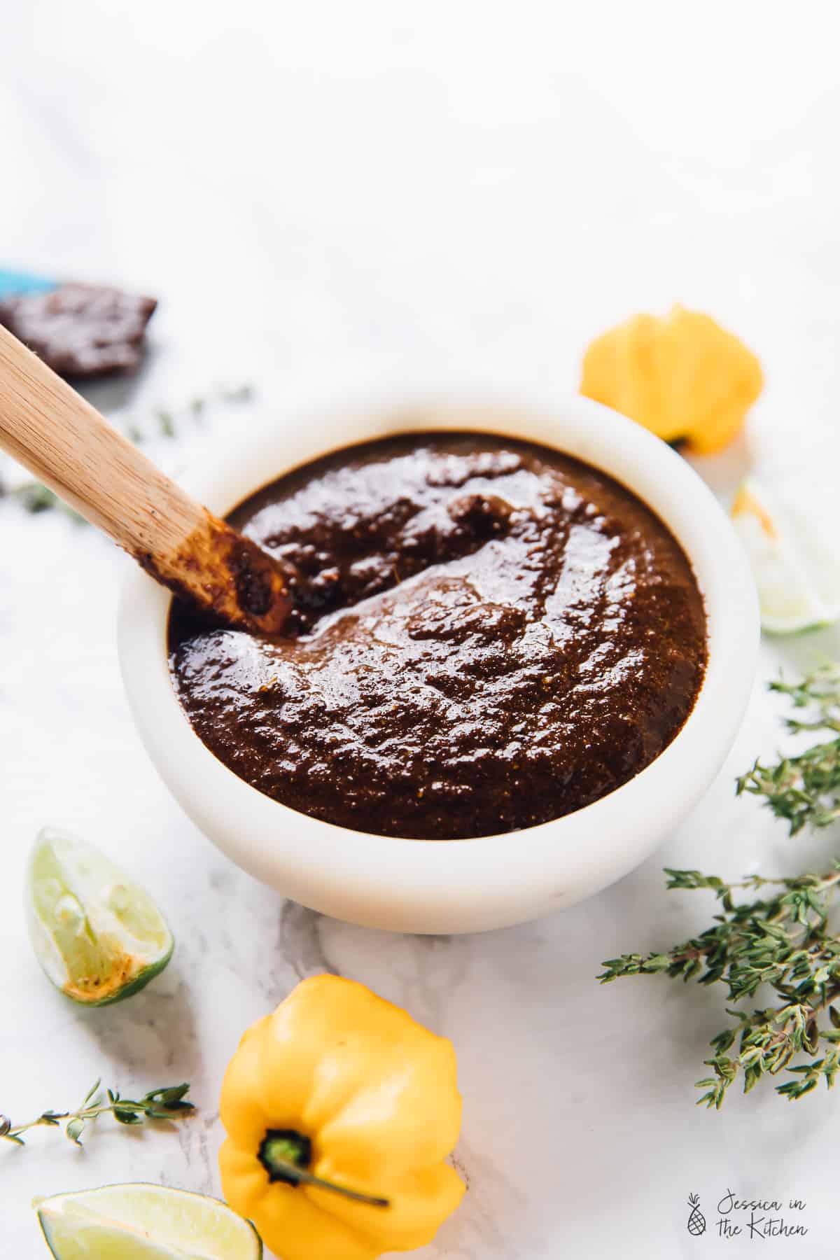 Jamaica Jerk Sauce in a small white bowl surrounded by scotch bonnet peppers.